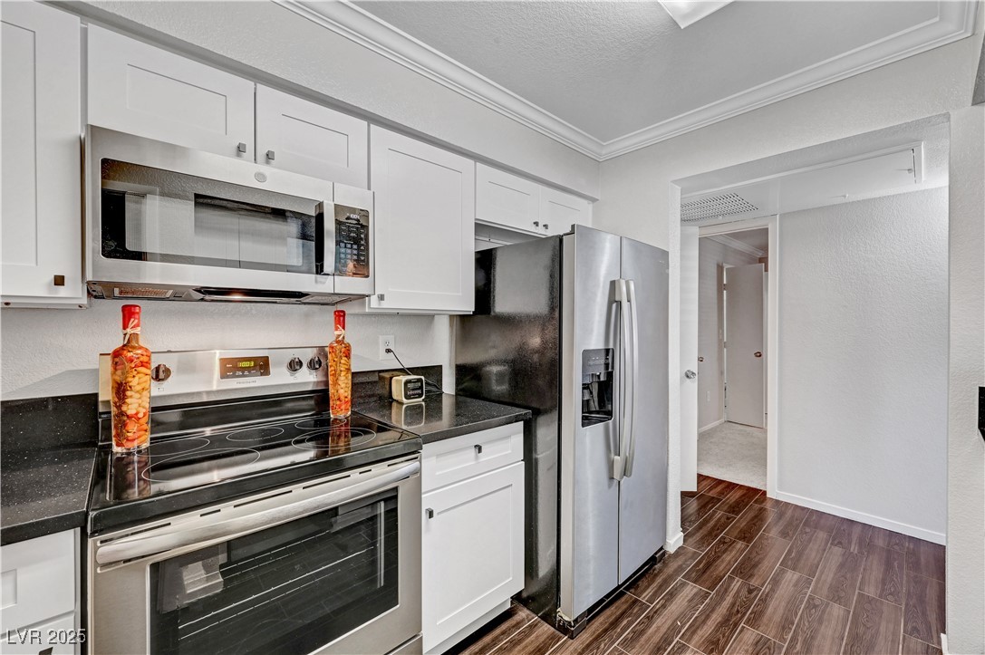 8101 West Flamingo Road, Unit 1163 Las Vegas, NV 89147 - Photo 13 of 45 Kitchen featuring stainless steel appliances, wood tiled floors, crown molding, white cabinetry, and a textured ceiling