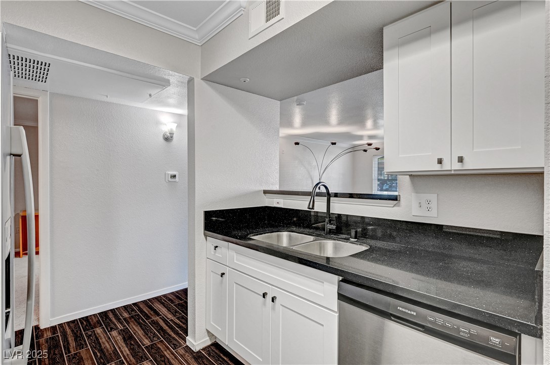 8101 West Flamingo Road, Unit 1163 Las Vegas, NV 89147 - Photo 14 of 45 Kitchen featuring dark stone counters, wood finish floors, stainless steel dishwasher, white cabinets, and ornamental molding