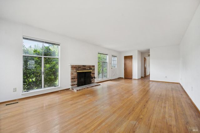 an empty room with wooden floor fireplace and windows