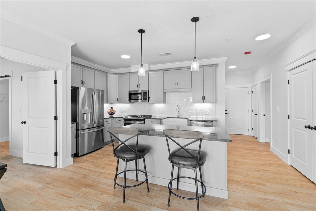 57 Long Point Road, Unit 310 Lakeville, MA 02347 - Photo 7 of 21 a kitchen with stainless steel appliances kitchen island granite countertop a refrigerator a stove a sink dishwasher and white cabinets with wooden floor