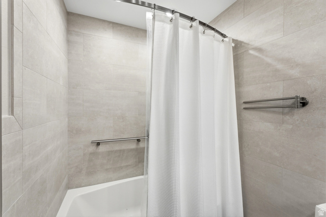 2073 Village Point Way Sandy, UT 84093 - Photo 47 of 68 Bathtub with light-toned wall tiling, a curved shower rod, and a wall-mounted towel bar