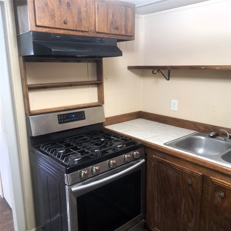 397 Lacy Drive, Unit B Elgin, TX 78621 - Photo 2 of 19 Kitchen featuring gas range, open shelves, exhaust hood, and dark brown cabinetry
