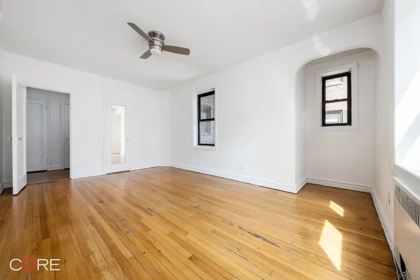 an empty room with wooden floor chandelier and windows