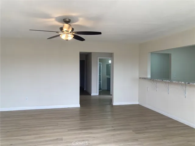 a view of an empty room with wooden floor and a ceiling fan