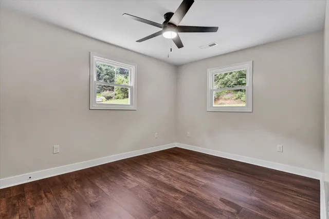 a view of an empty room with wooden floor and a ceiling fan