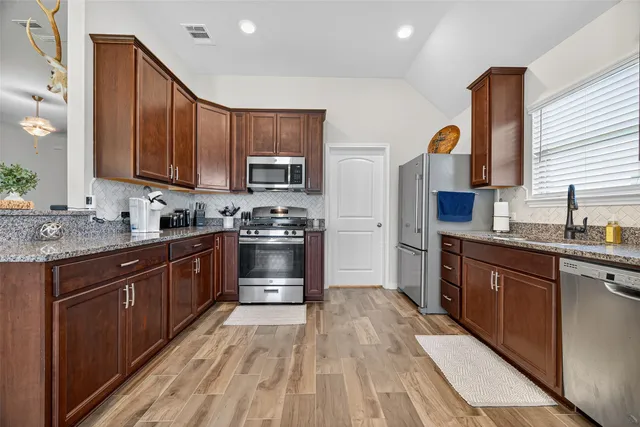 a kitchen with stainless steel appliances granite countertop wooden cabinets a stove top oven a sink and dishwasher with wooden floor