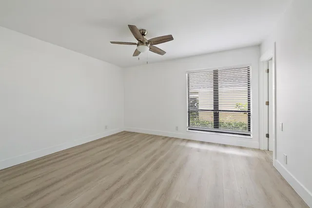 an empty room with wooden floor fan and windows