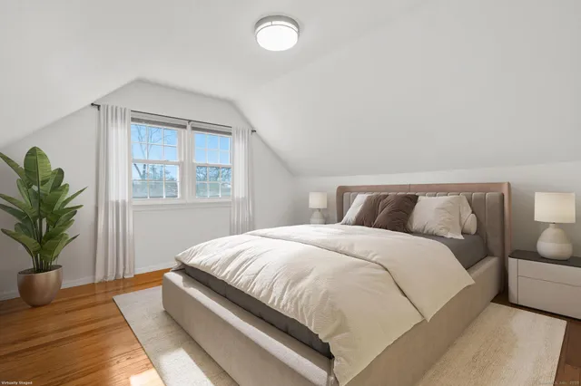 a bedroom with a large bed and potted plant with wooden floor
