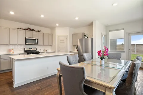 a kitchen with kitchen island granite countertop a dining table chairs refrigerator and microwave