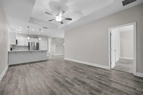 a view of an empty room and kitchen view with wooden floor