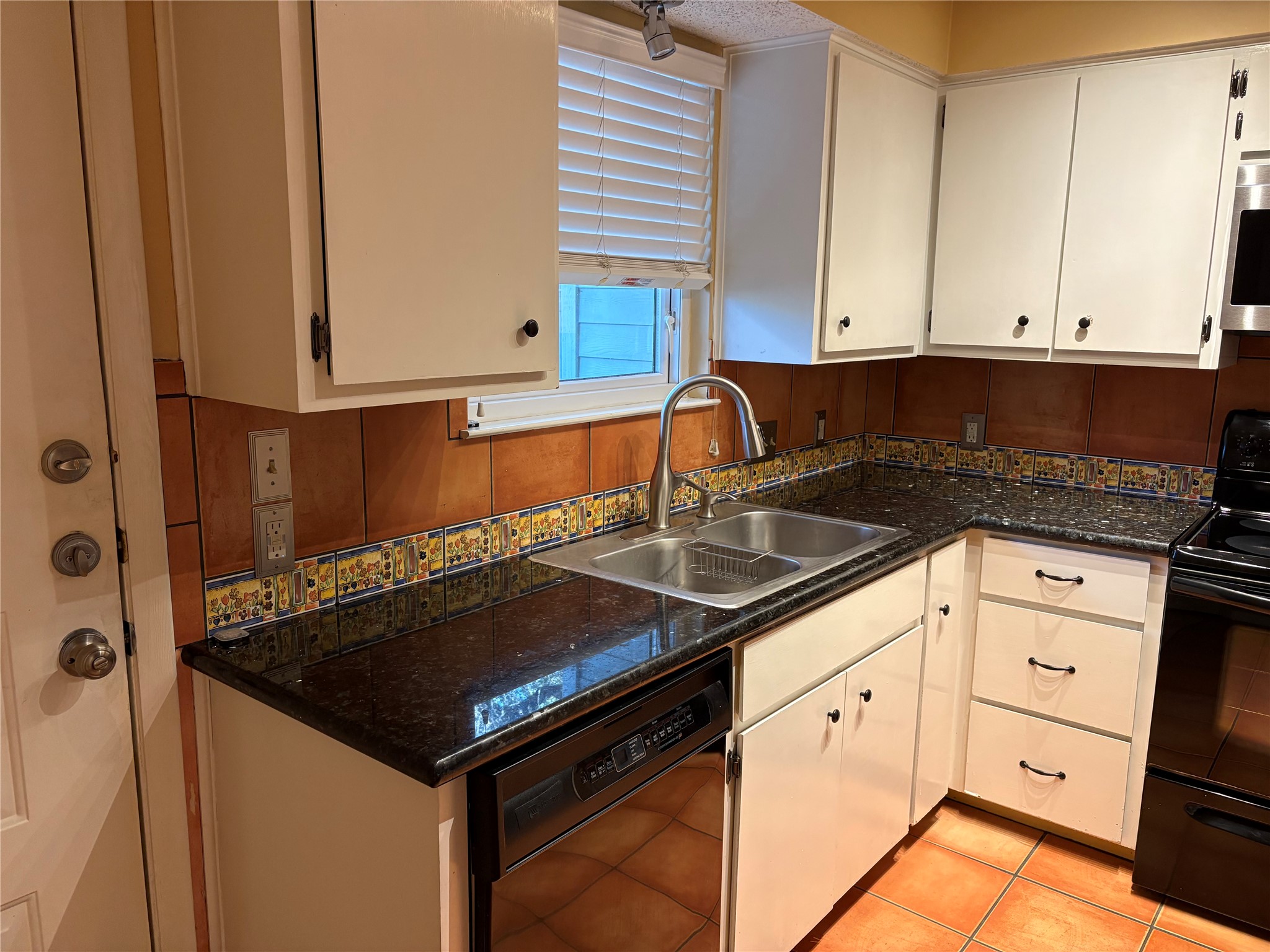 9226 Jollyville Road, Unit 144 Austin, TX 78759 - Photo 10 of 40 Kitchen with black appliances, dark stone counters, light tile patterned flooring, and white cabinetry