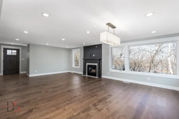an empty room with wooden floor fireplace and windows