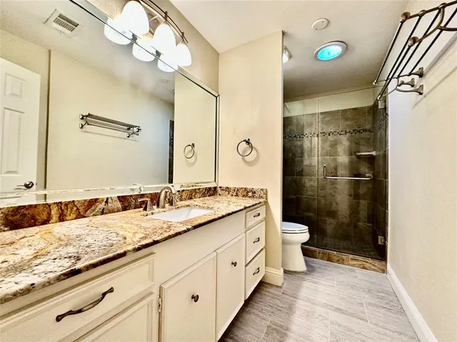 a bathroom with a granite countertop sink a toilet a mirror and shower