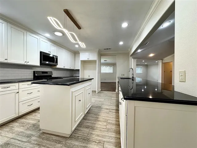 a large white kitchen with stainless steel appliances granite countertop a sink a stove and a refrigerator