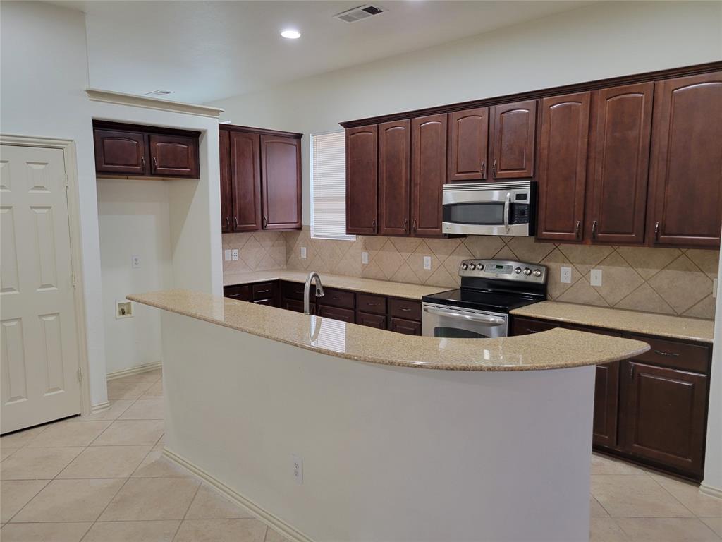 508 Hummingbird Drive Little Elm, TX 75068 - Photo 3 of 14 a kitchen with kitchen island granite countertop a sink a stove a microwave and wooden cabinets