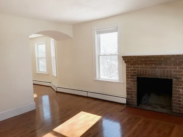 an empty room with wooden floor fireplace and windows