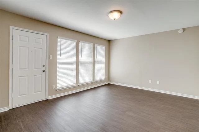 an empty room with wooden floor and windows with curtains
