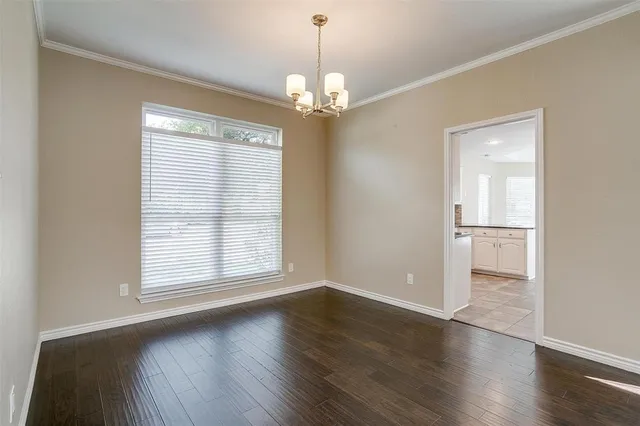 an empty room with wooden floor chandelier and windows