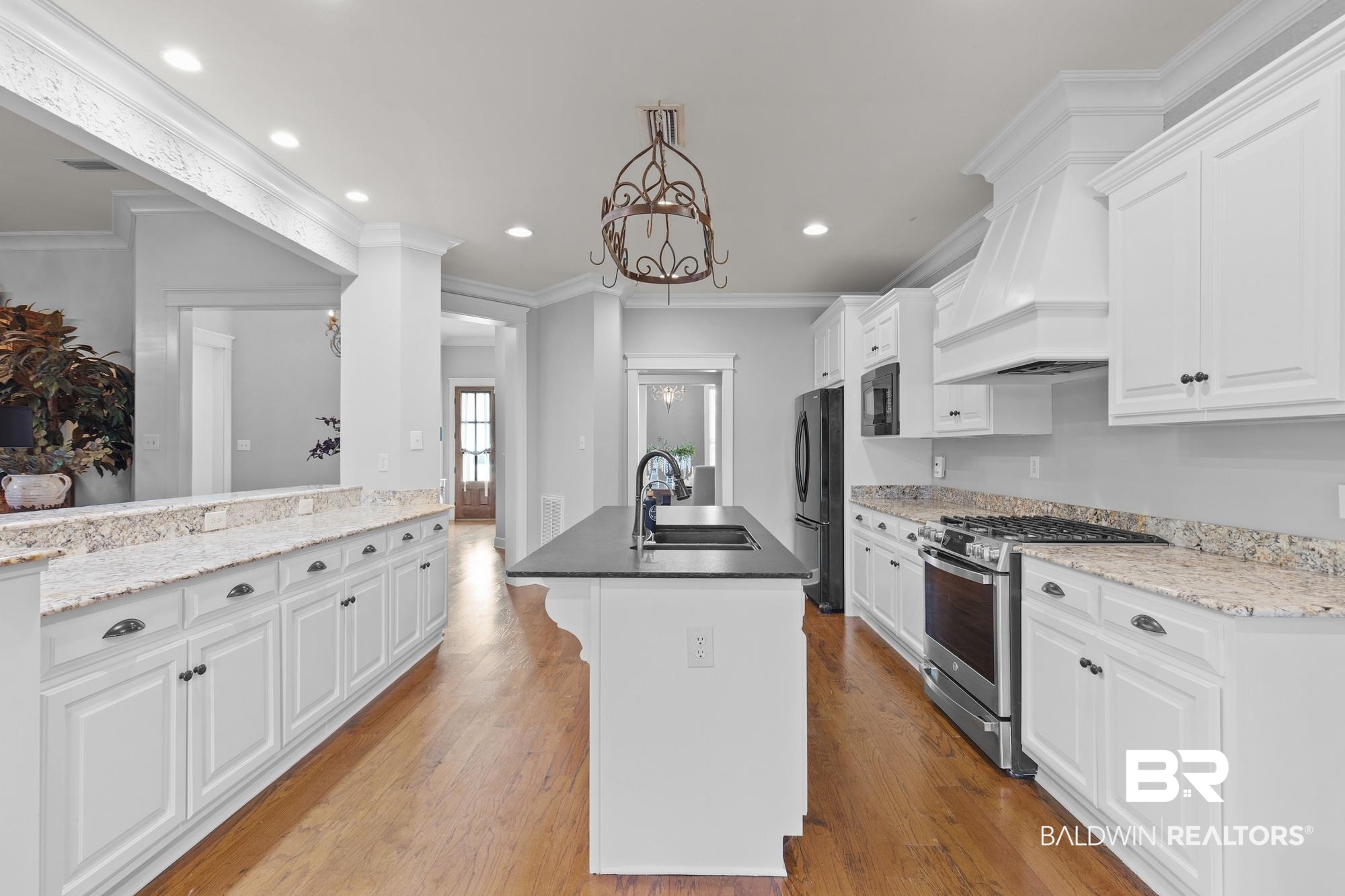 11261 Halcyon Loop Daphne, AL 36526 - Photo 10 of 41 Gourmet kitchen with a central island featuring an undermount sink, white cabinetry with dark hardware, stainless steel appliances, light-toned granite countertops, and hardwood flooring
