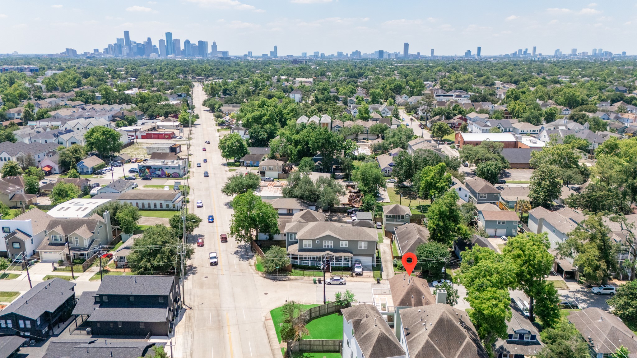 6621 North Main Street Houston, TX 77009 - Photo 36 of 41 This aerial photo showcases a suburban neighborhood with tree-lined streets and a clear view of a distant city skyline. The area features a mix of residential homes, some with lush green yards, and is marked by a red pin indicating a specific property. It's a blend of urban convenience and suburban tranquility.