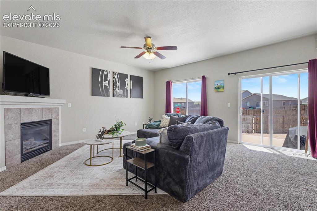 6598 Alliance Loop Colorado Springs, CO 80925 - Photo 5 of 39 Living area featuring a gas fireplace with a tiled surround, a ceiling fan, and sliding glass doors leading to the exterior