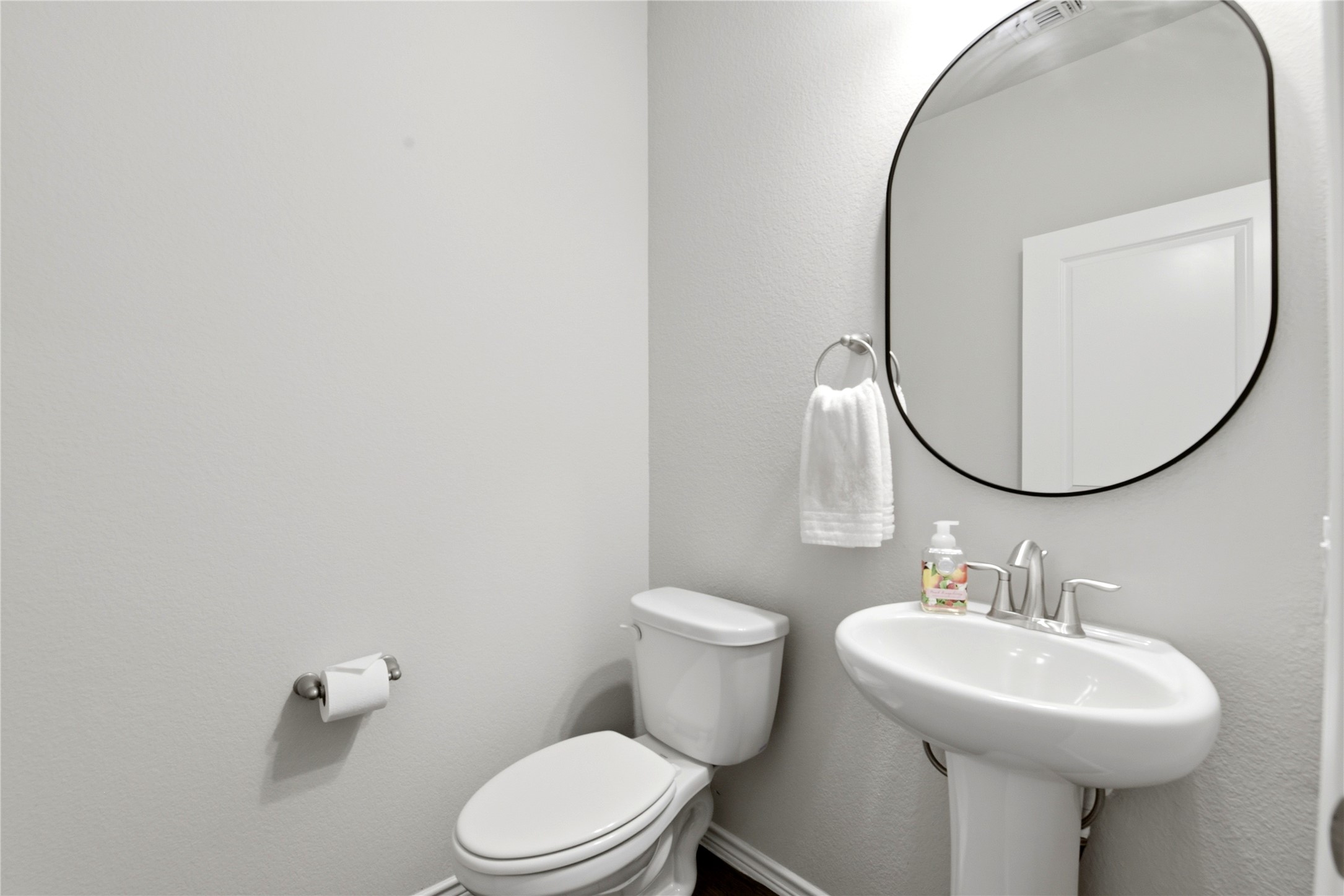 17834 Maple Ash Drive Spring, TX 77379 - Photo 25 of 50 This is a modern, minimalist 1/2 bathroom with neutral tones. It features a pedestal sink with a sleek faucet, a round mirror, and a toilet.