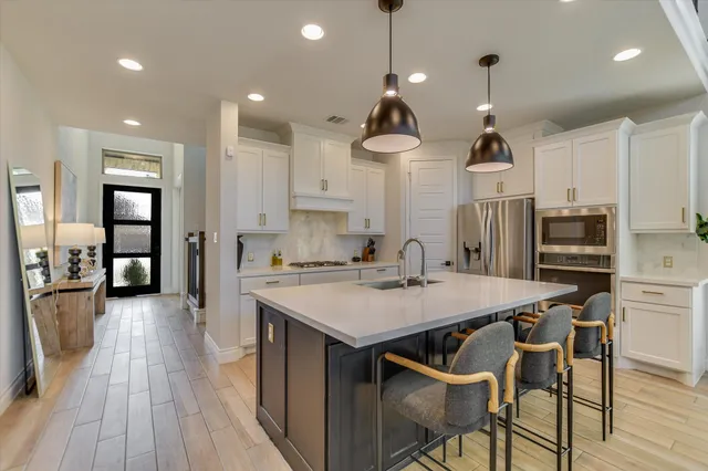 a kitchen with stainless steel appliances kitchen island granite countertop a stove a refrigerator a sink a dining table and chairs with wooden floor