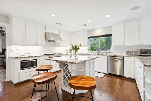 a kitchen with white cabinets a sink a stove a dining table and chairs