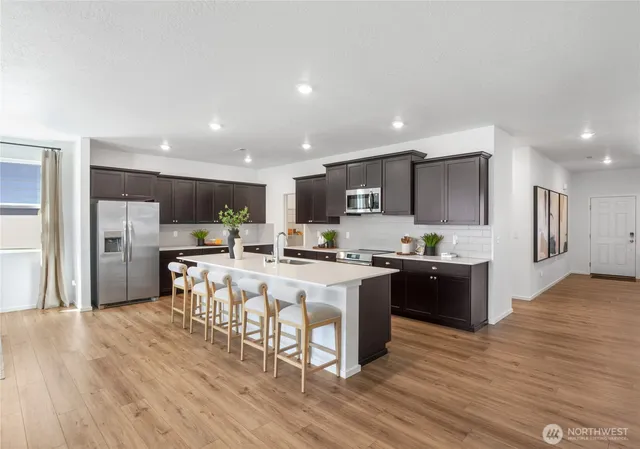 a kitchen with stainless steel appliances kitchen island granite countertop a stove top oven a sink a refrigerator and white cabinets with wooden floor
