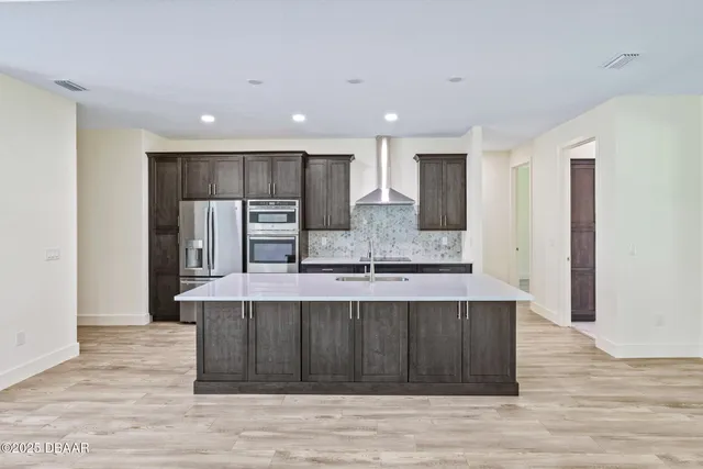 a large kitchen with stainless steel appliances a large counter top and wooden floors