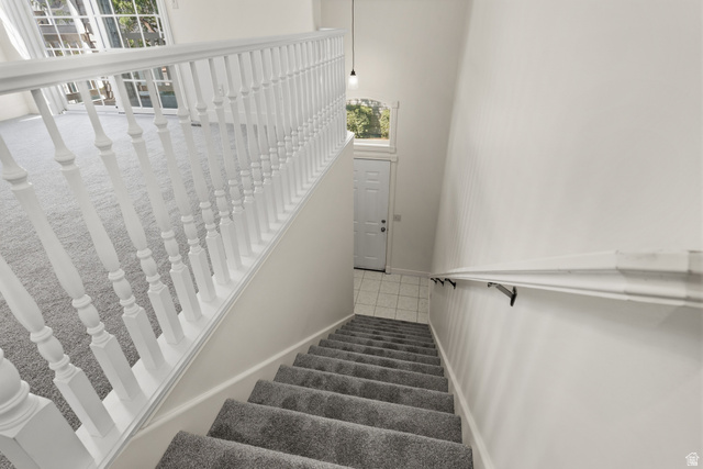 Carpeted staircase with white balusters and handrail, leading to a tiled entry with a white door and transom window