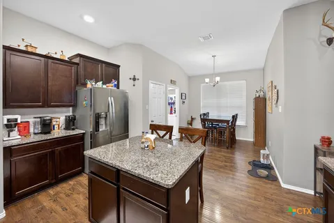 a kitchen with stainless steel appliances granite countertop a stove refrigerator a dining table and chairs with wooden floor