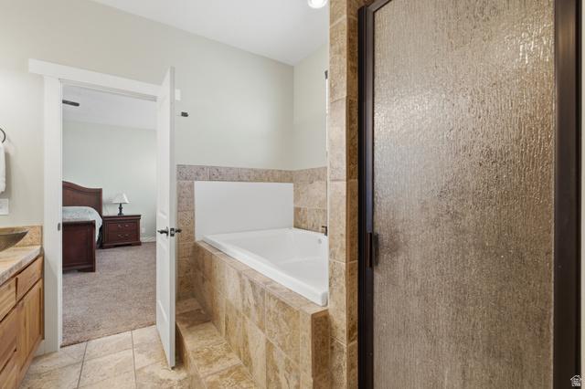 2567 West Rim Rock Drive Stockton, UT 84071 - Photo 26 of 64 Tiled shower with obscure glass door, integrated built-in bathtub, natural stone tile surround, and coordinating floor tiles