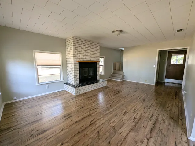 an empty room with wooden floor fireplace and windows