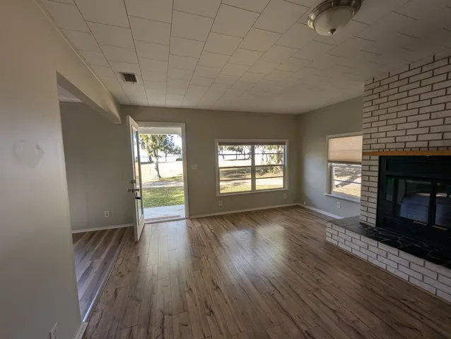 an empty room with wooden floor fireplace and windows