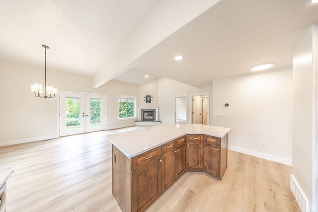 2169 Orchard Pines Loop East Bountiful, UT 84010 - Photo 7 of 32 Spacious open concept interior featuring a large kitchen island with wood-finish cabinetry and light-toned countertop, wood-finish flooring, a vaulted ceiling, and a fireplace with a light-toned hearth