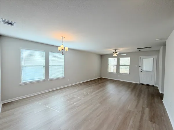 an empty room with wooden floor chandelier and windows
