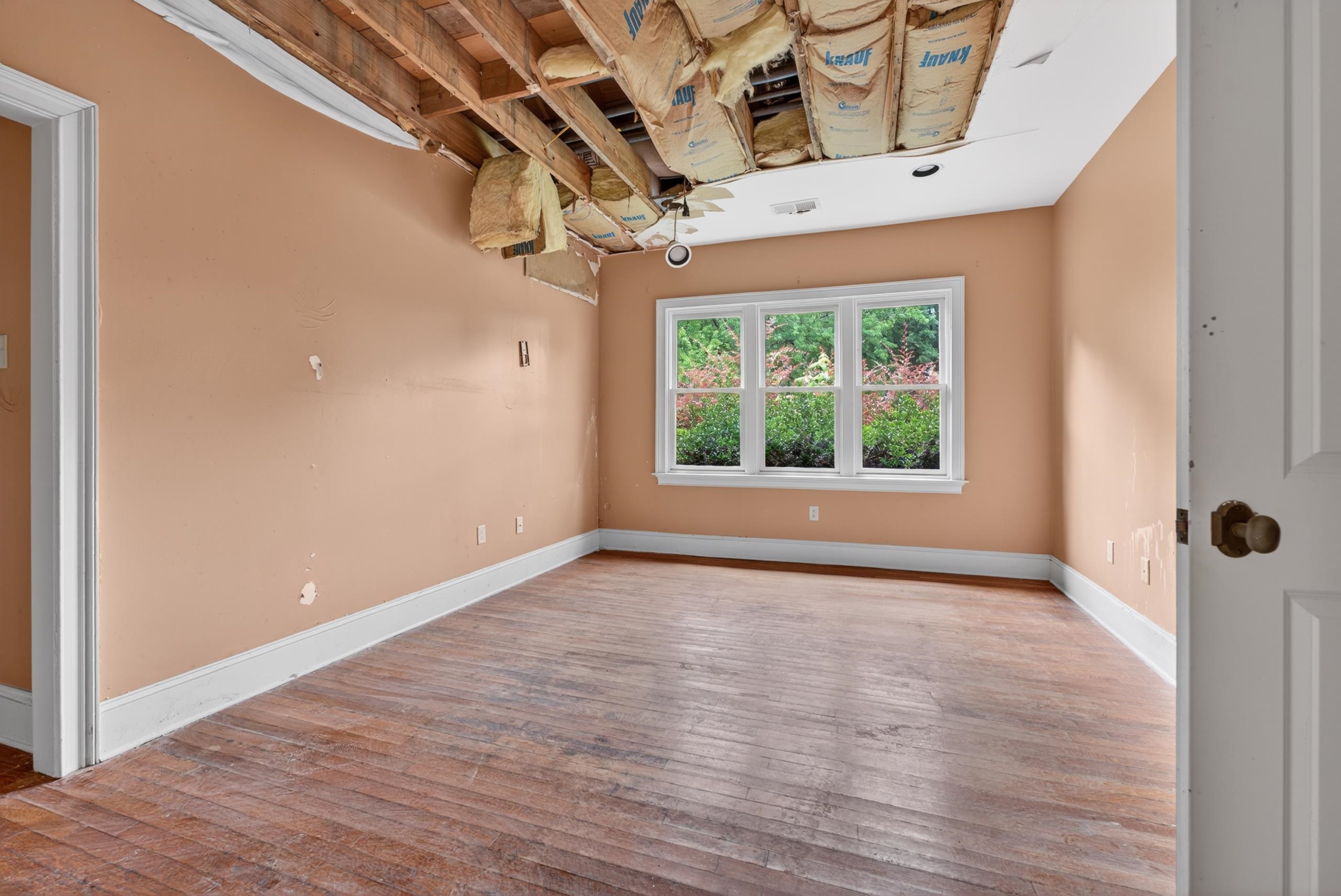 530 West Raines Road Memphis, TN 38109 - Photo 27 of 38 Room featuring wood flooring, three-panel window, baseboard molding, and an exposed ceiling structure with insulation
