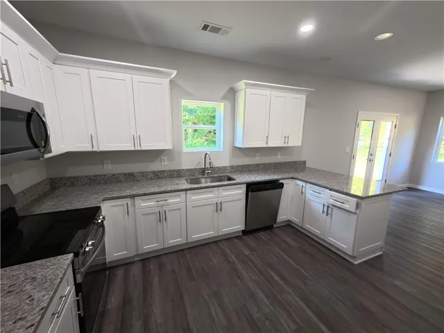 a kitchen with granite countertop white cabinets a sink a window and wooden floors