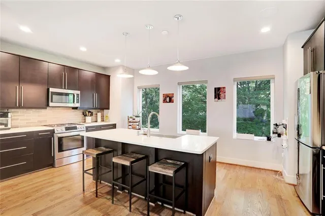 a open kitchen with stainless steel appliances granite countertop a stove top oven a sink dishwasher a dining table and chairs with wooden floor