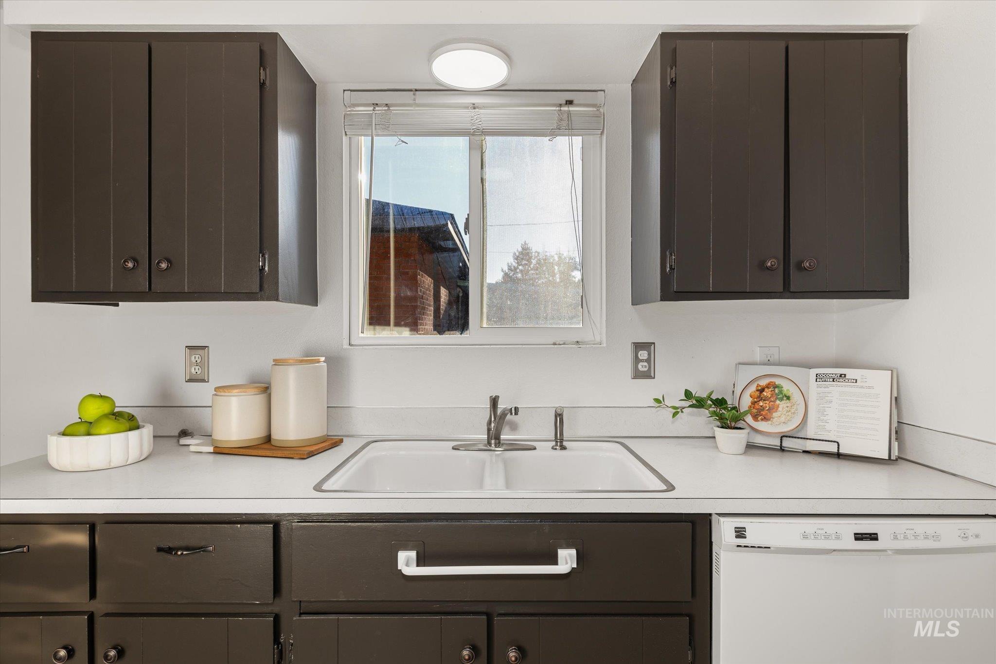 2302 Pendleton Street Boise, ID 83705 - Photo 17 of 35 Kitchen featuring dark cabinetry, a double basin sink with a chrome faucet, a window with blinds, a white countertop, and a built-in dishwasher