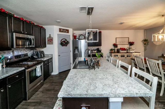 a kitchen with stainless steel appliances granite countertop a stove top oven a sink dishwasher a dining table and chairs with wooden floor