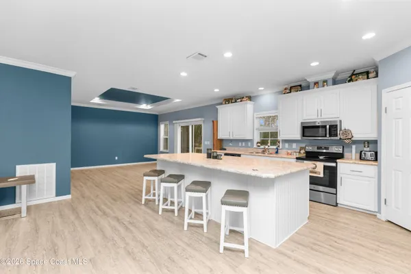 a kitchen with stainless steel appliances kitchen island granite countertop a stove a sink a refrigerator and white cabinets with wooden floor