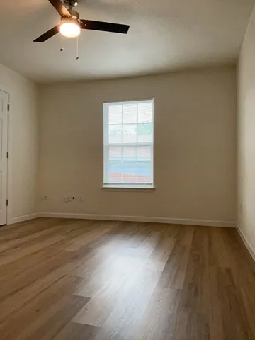 an empty room with wooden floor chandelier fan and windows