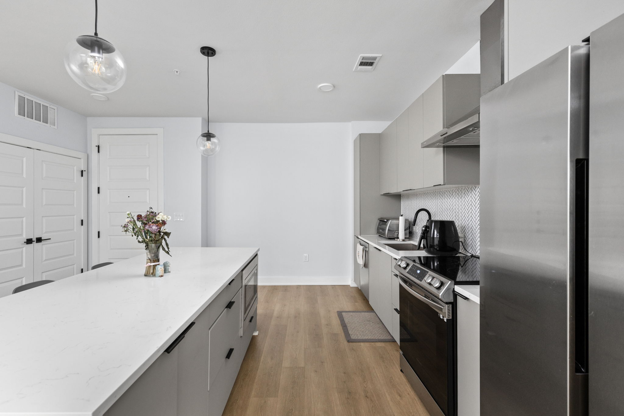 2500 Longview Street, Unit 405 Austin, TX 78705 - Photo 7 of 28 Dual tone kitchen with stainless steel appliances, two tone color scheme, decorative light fixtures, light wood-style flooring, and modern cabinets