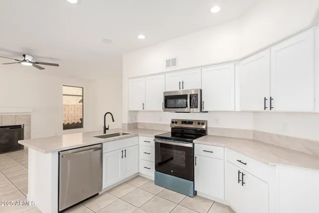 a kitchen with stainless steel appliances granite countertop white cabinets a sink a stove a microwave and a refrigerator