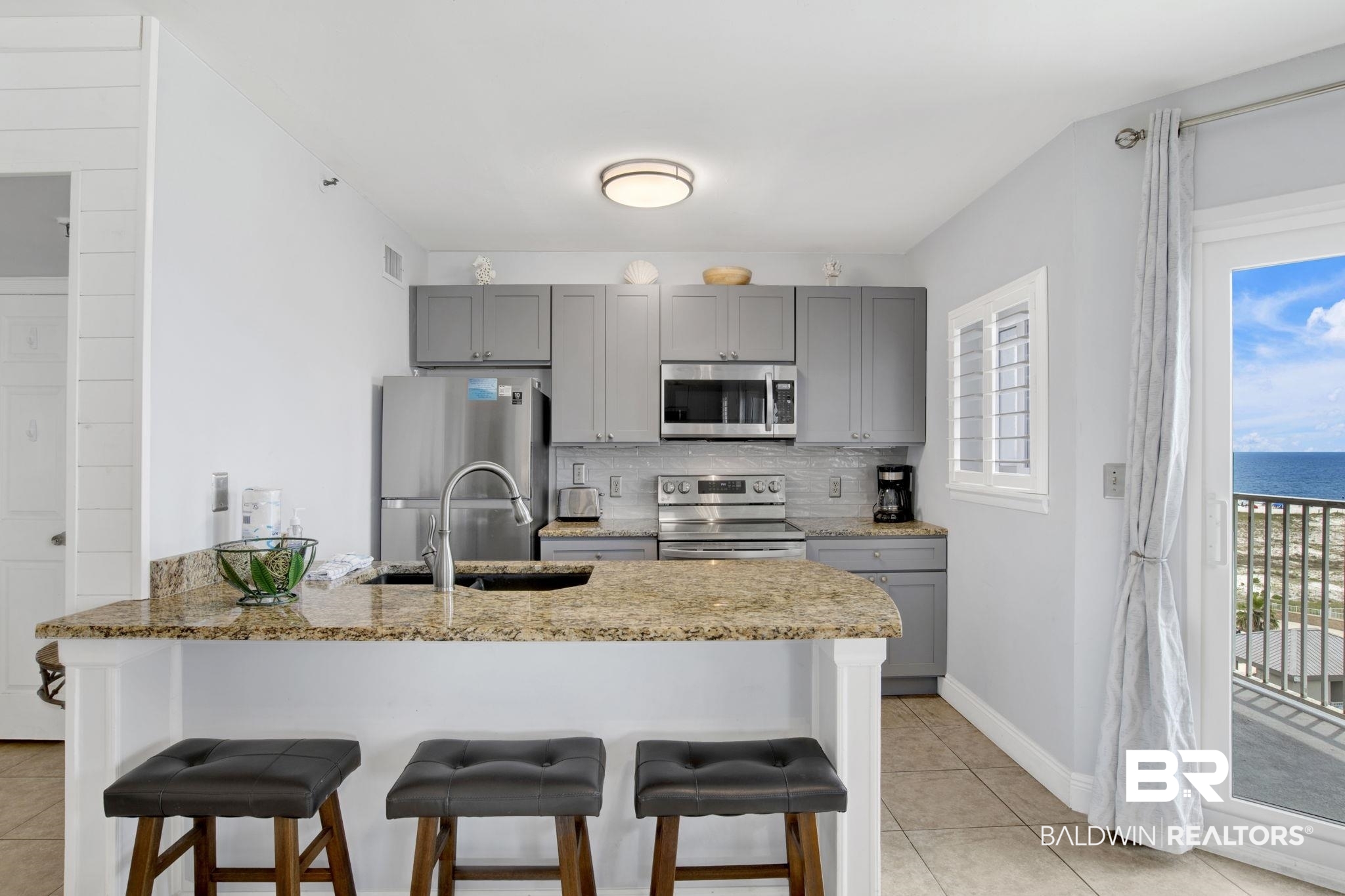 375 Plantation Road, Unit 5514 Gulf Shores, AL 36542 - Photo 17 of 44 Kitchen with appliances with stainless steel finishes, gray cabinetry, a kitchen breakfast bar, light tile patterned flooring, and backsplash