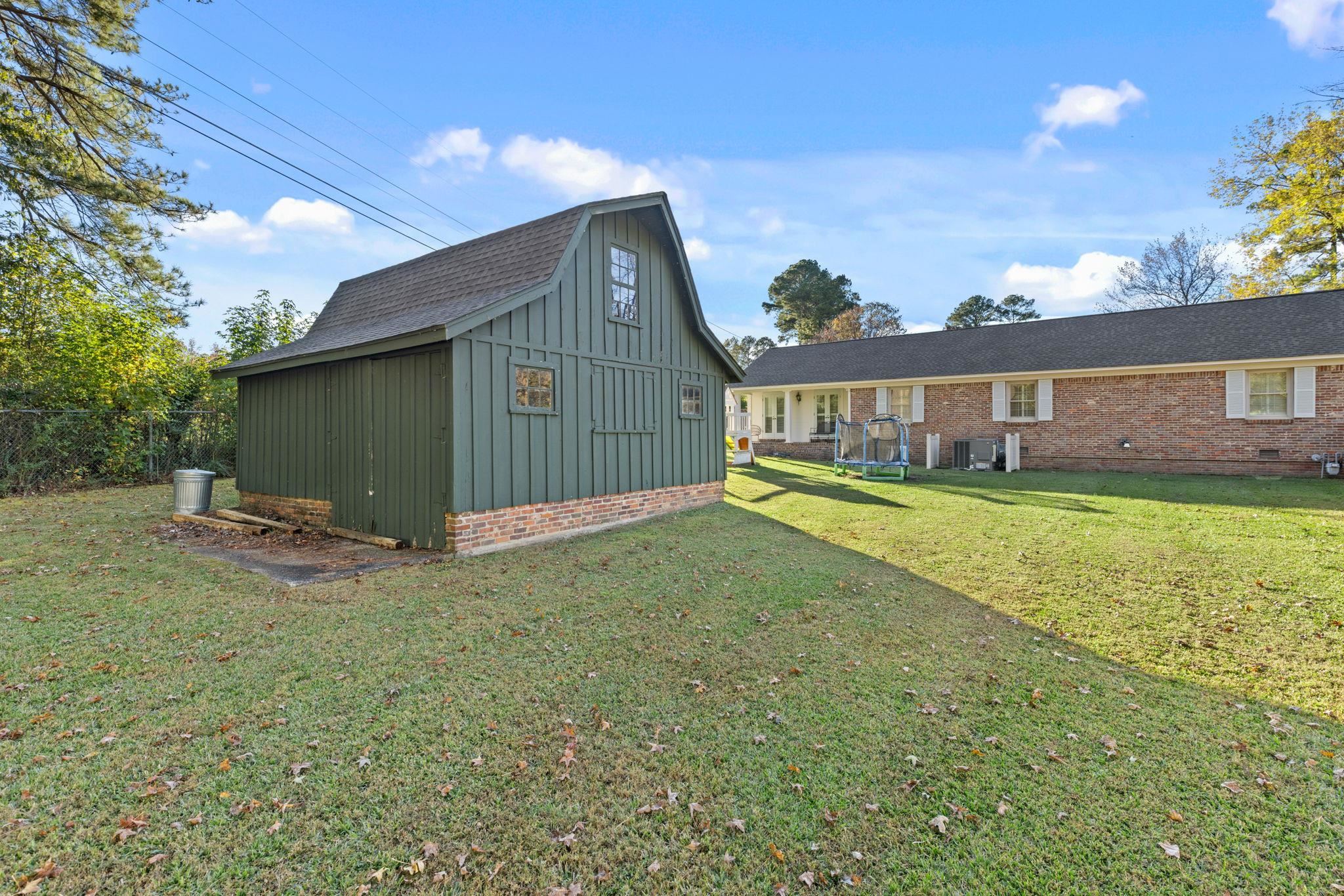 1201 West Clover Lane Corinth, MS 38834 - Photo 18 of 35 Back of house featuring an outbuilding, a yard, board and batten siding, a trampoline, and brick siding