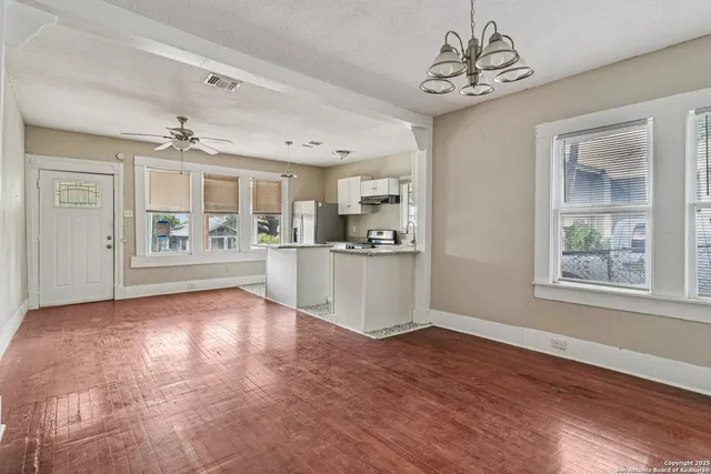 a view of an empty room with kitchen and window