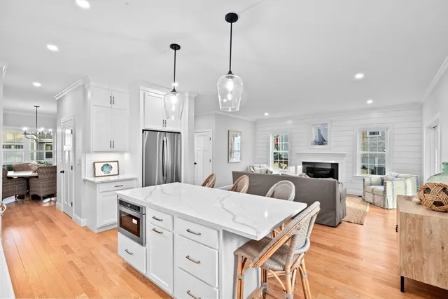 a kitchen with stainless steel appliances kitchen island granite countertop a refrigerator a stove top oven a sink a dining table and chairs with wooden floor